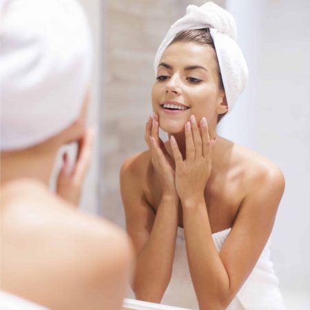 woman in towel looking at herself in mirror touching face